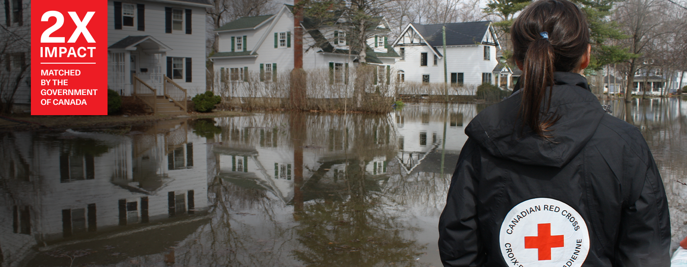 Woman in Red Cross jacket looking at houses on a flooded street