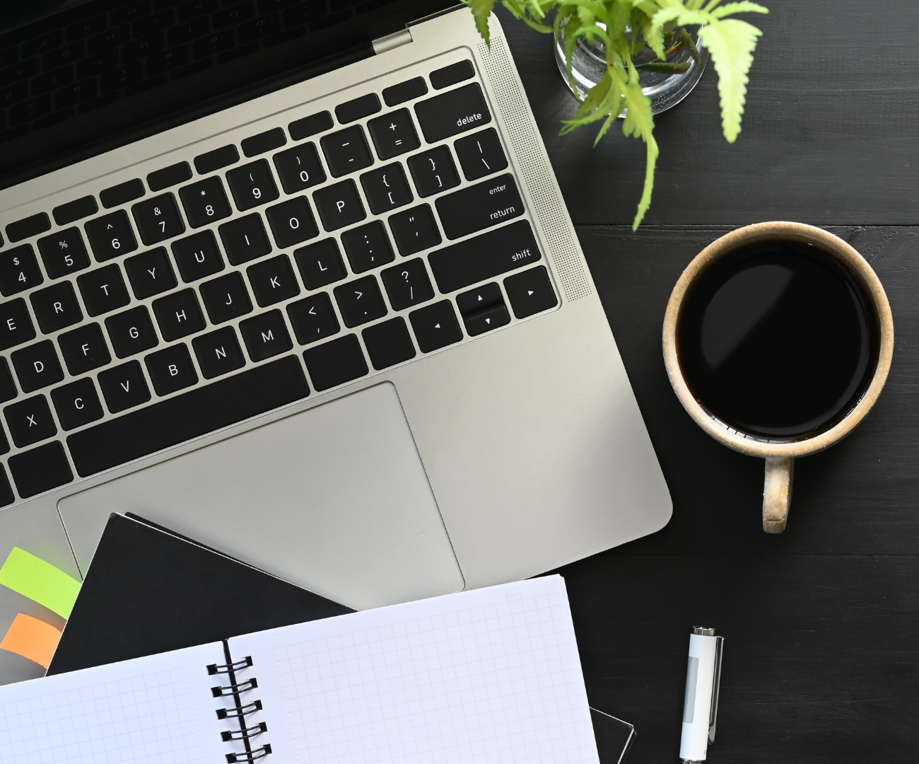 an open laptop, an open notebook, a mug of black coffee